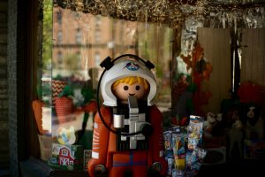 Astronaut Playmobil Figure with Spaceshuttle Sticker on it´s helmet surrounded by cheap looking packaged toys and strawberryish school cones